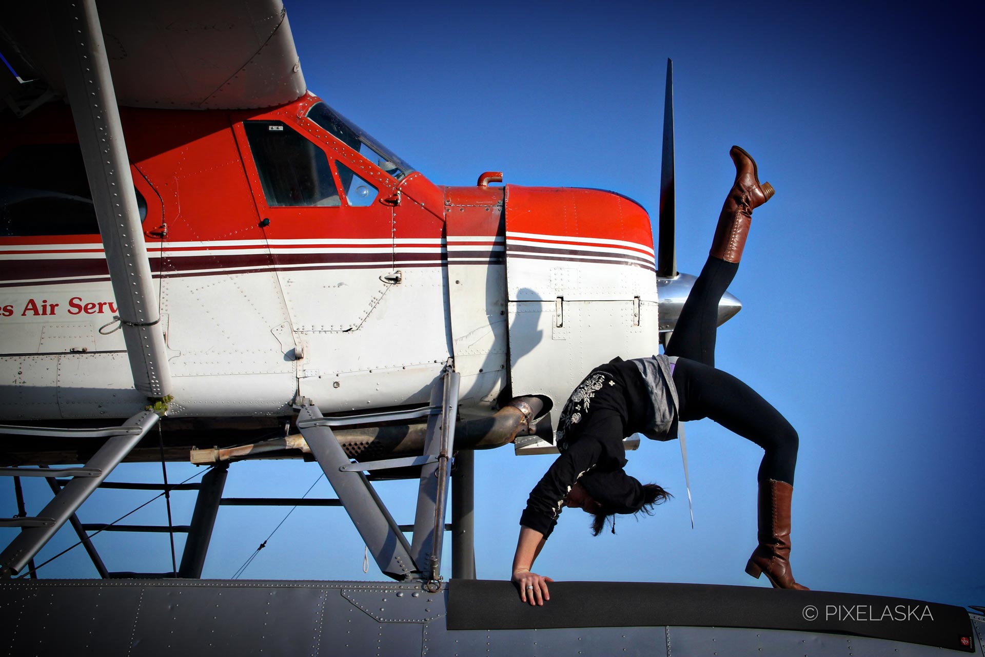 A woman dressed in black poses in a backbend atop the float of a white and red Beaver floatplane in Fairbanks, Alaska, to illustrate her career as a pilot and a yoga instructor. Personal Branding photos by Heather Taggard, 49 designs and Pixelaska.